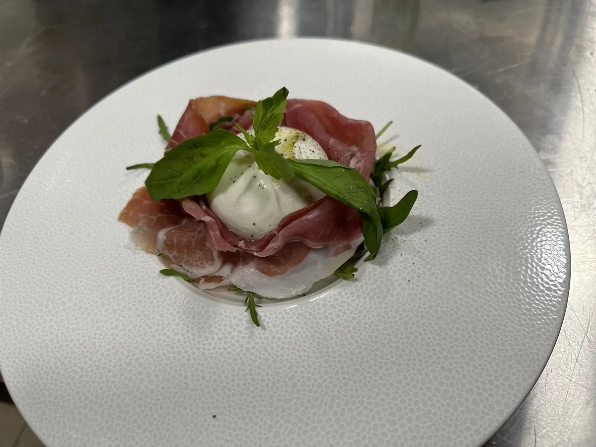 Prosciutto and burrata topped with fresh basil on a wide white dish