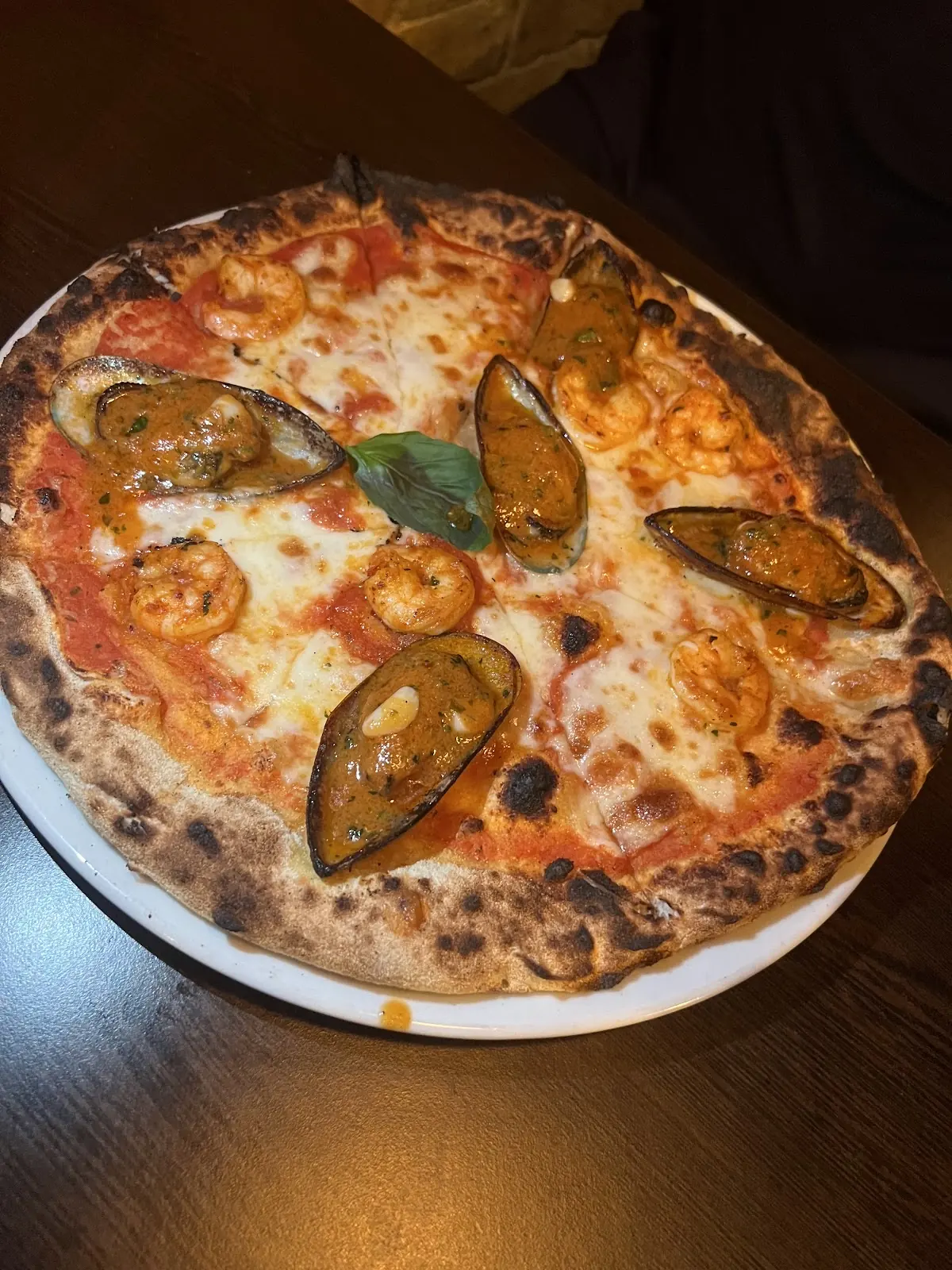 A tomato and mozzarella pizza topped with mussels in the shell and basil, in warm low light