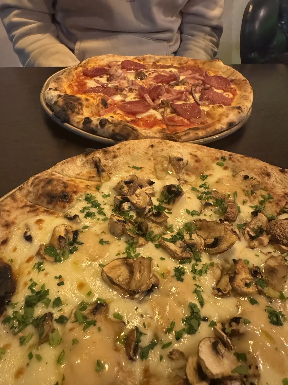 Two pizzas on a table, a mushroom white pizza in front and a tomato pizza behind